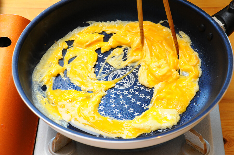 卵焼きを作ります。ボウルにたまごを割り入れて白だしを加えて混ぜ合わせます。中火に熱した卵焼き器にサラダ油をひいて卵を入れたら、大きくかき混ぜて半熟状になったら半分に折り、火から下ろして半分に切ります。