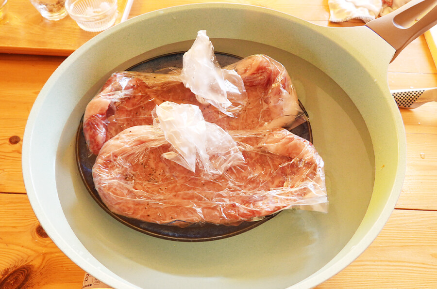 フライパンに、皿を敷いて（直接ポリ袋に火が当たらないように）肉が隠れるくらい水を注ぎます。