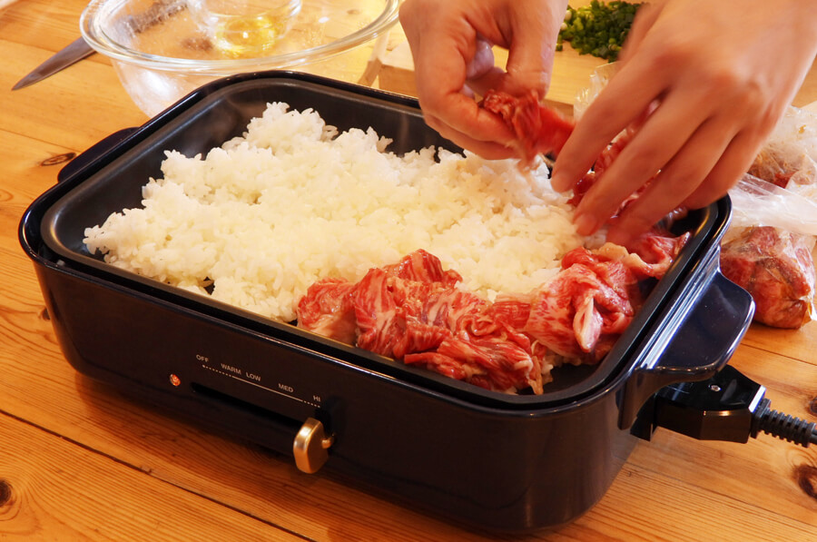 ホットプレートにオリーブオイルを入れて中央にごはんを置いて、その周りに肉を並べます。